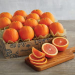 A photo of honeybell oranges in a box with several sliced on a cutting board in front