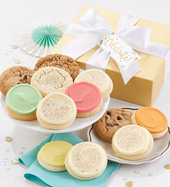 A photo of birthday gift ideas with two plates of cookies in front of a gold box with a white ribbon.