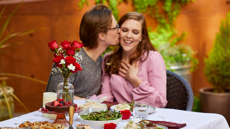 A photo of Valentine's Day Gifts for Her with a couple having a dinner outside with the man kissing the woman's cheek